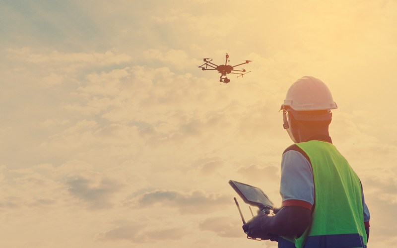 A worker wears a safety vest and hardhat while flying an Uncrewed Aircraft Systems (UAS)