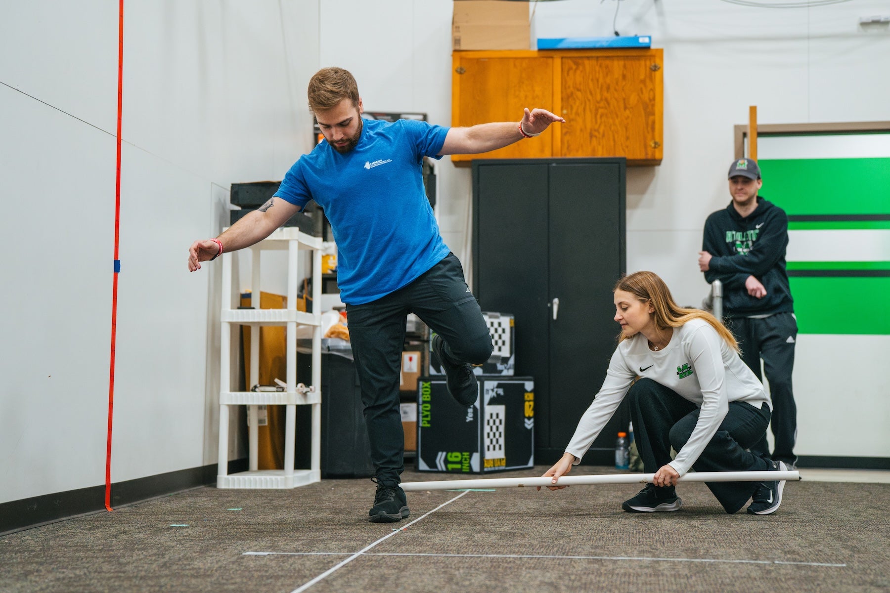 student balancing on a line on the floor and a professor and another student observing