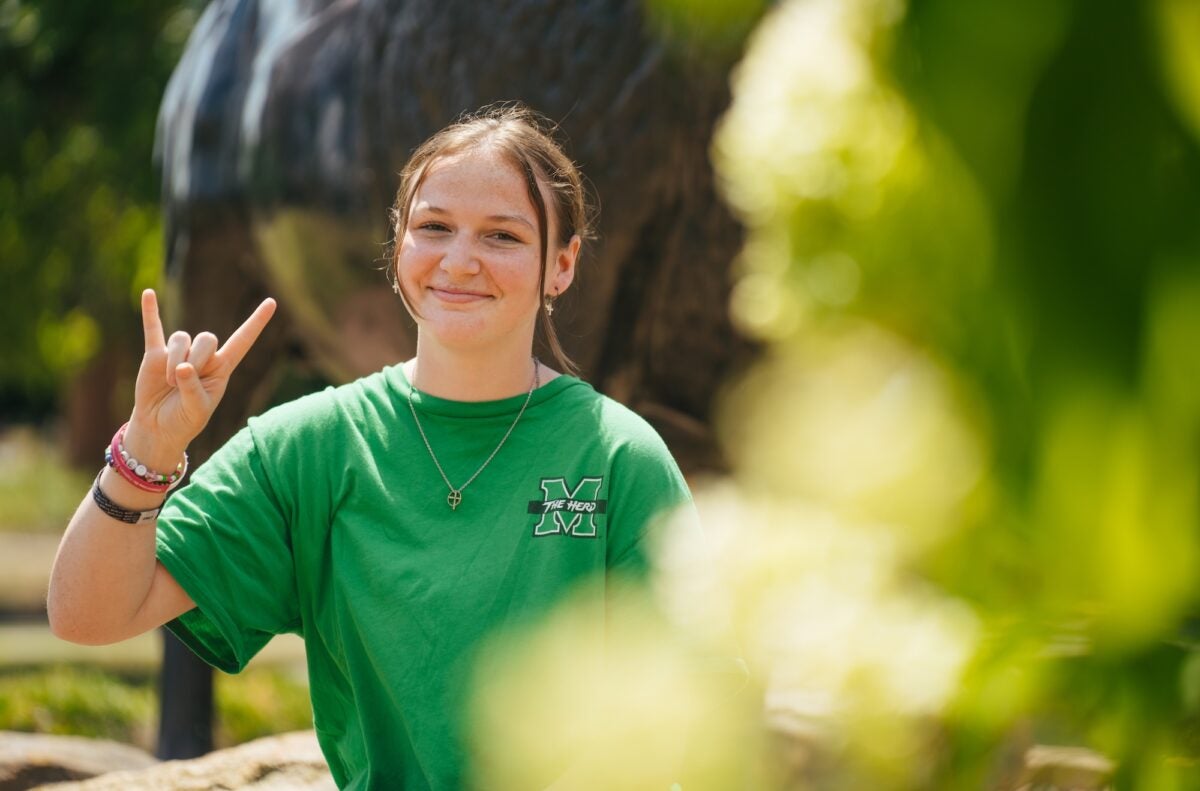 student on campus giving the Go Herd symbol with her hand