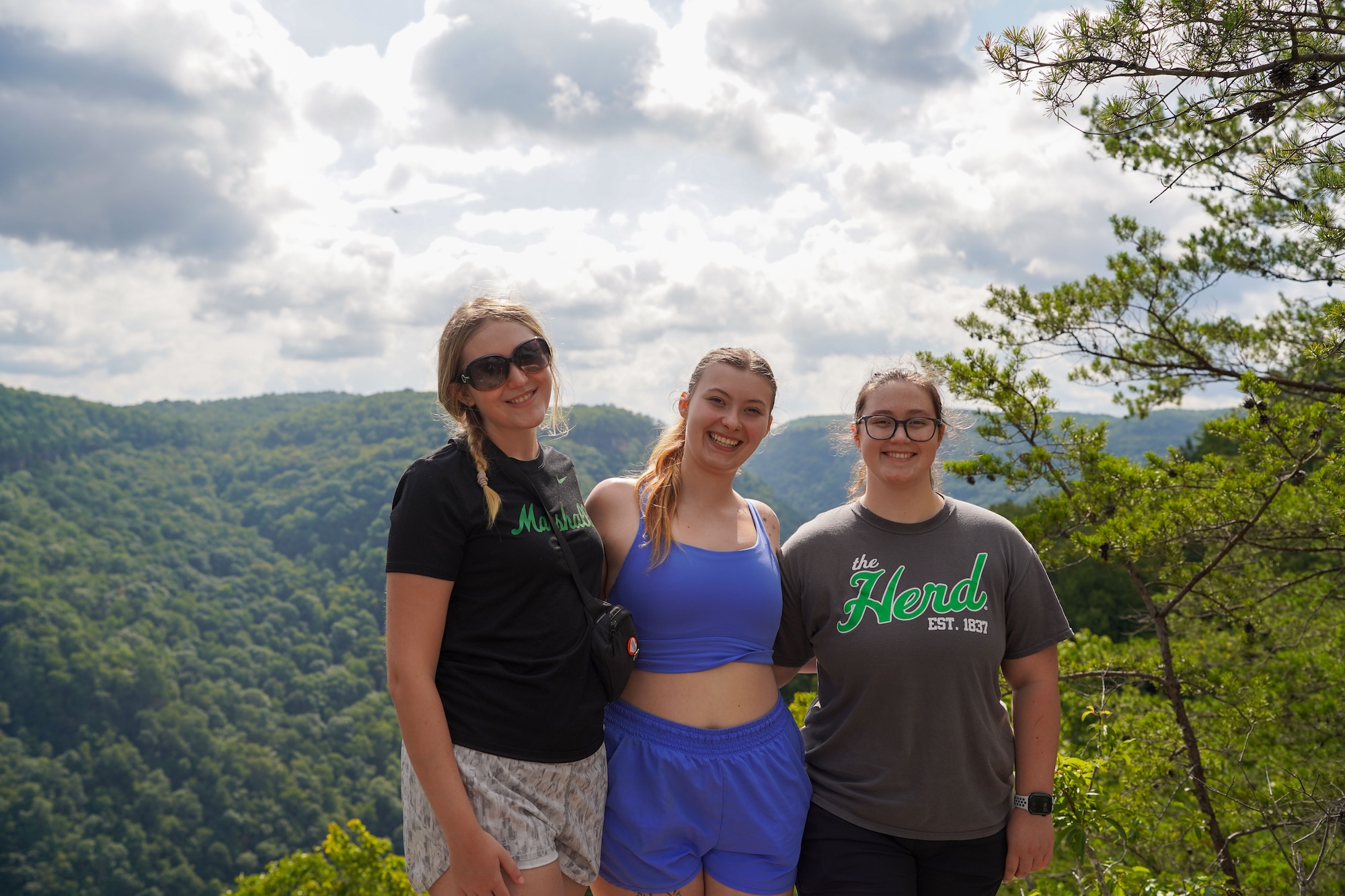 three scholars on a hike smiling at the camera
