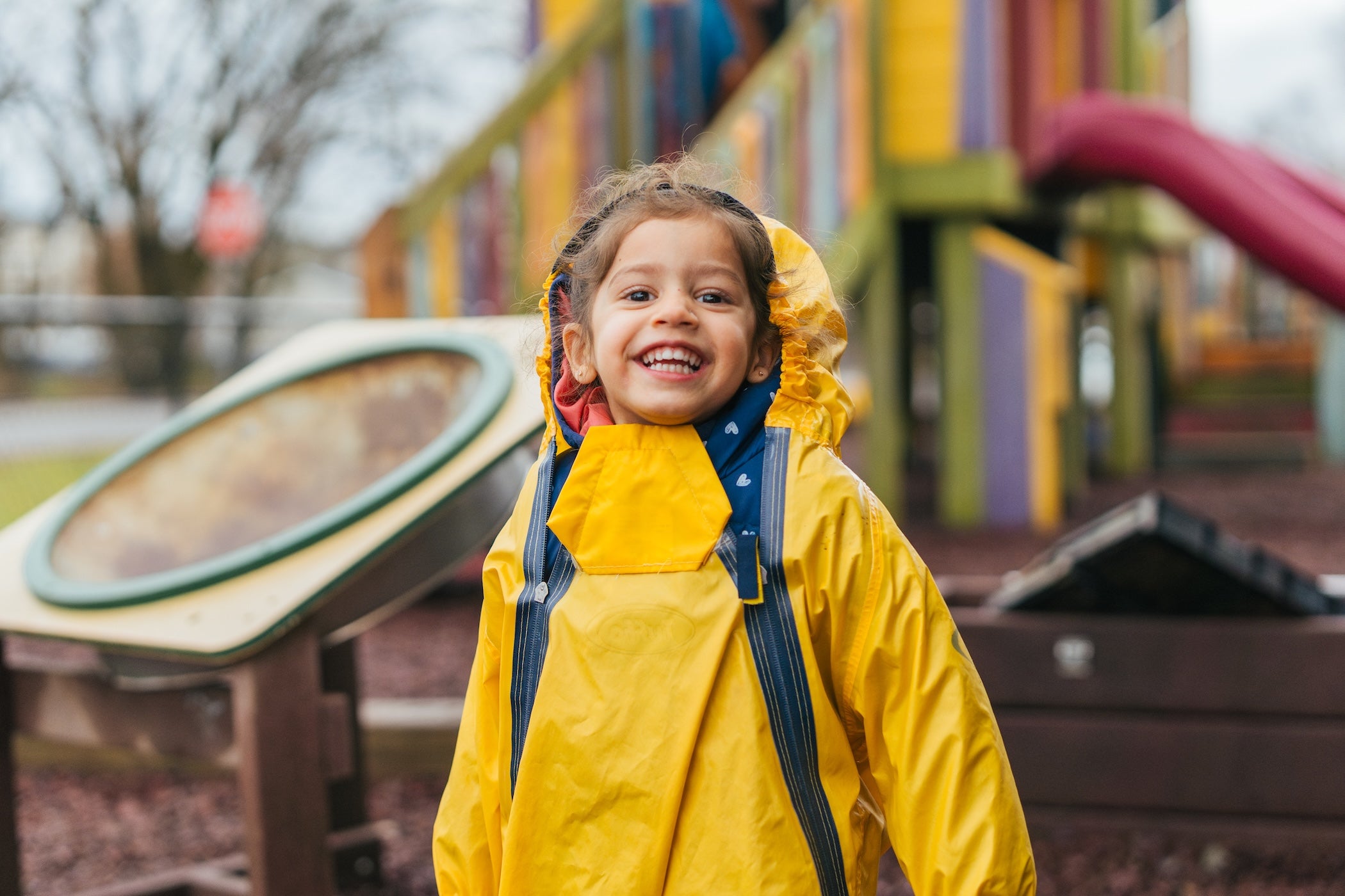 toddler smiling on the playground in a rainsuit