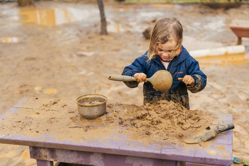 child in a rain suit playin in the mud with a ladle