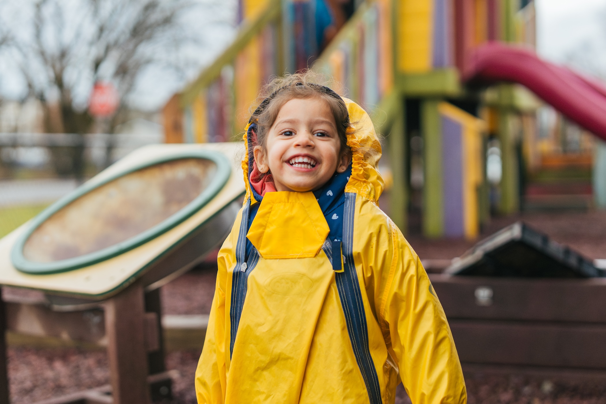 toddler smiling on the playground in a rainsuit