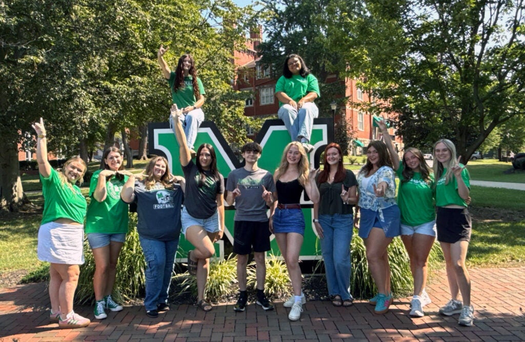 Marshall University's Social Media Ambassadors are all smiling while gathered around a large block M logo sign on Marshall's Huntington campus 