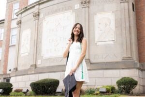 Biology student Asha Bora poses in front of the Science Building with her graduation regalia