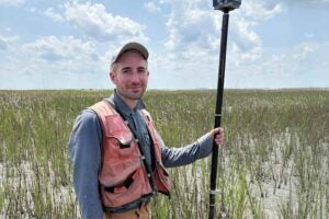 Biology graduate student Zak Bartholomew holding an instrument used in surveying coastal vegitation
