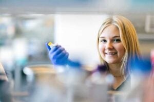 Student works in a laboratory, holding a small sample container while conducting hands-on science research.