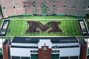 Aerial view of members of Marshall University's Class of 2030 standing on the field at Joan C. Edwards Stadium, arranged in the shape of the Marshall block M