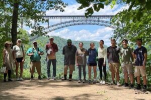 Participants in Marshall University's Appalachian Mathematics and Physics Site (AMPS) summer research program stand on a trail overlook at New River Gorge National Park with the New River Gorge Bridge in the background