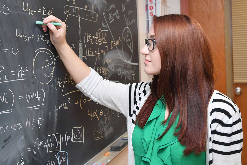 A physics student works diligently on a board full of equations, expanding her understanding