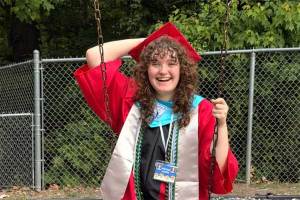 Payton wears her red cap and gown while swinging on the playground outside of her high school graduation