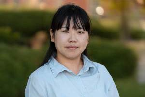 Headshot of Dr. Sachiko McBride outdoors, wearing a light blue button-down shirt, with blurred greenery in the background.