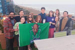 A group of Biology students take a moment to celebrate their work with a group picture holding a green Marshall University flag at a rooftop beach-side restaurant during a conference in Myrtle Beach, SC