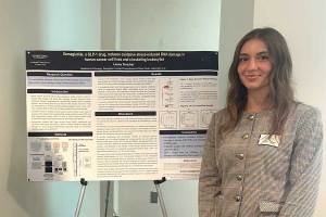 Biological sciences student Laney Fletcher stands beside a research poster presenting cancer research conducted during Georgetown University's Cancer Undergraduate Research Experience and Mentorship (CURE-M) program.