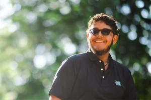 Cyber Forensics and Security student Dominick Barham stands outdoors on campus wearing a Marshall University polo shirt and sunglasses