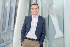 Chemistry alumnus Ethan Adkins stands beside a glass wall celebrating his successful doctoral defense
