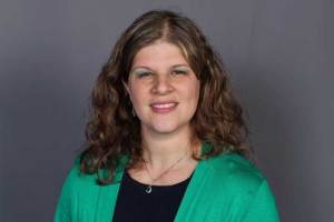 Professional headshot of Dr. Rosalynn Quiñones wearing a green cardigan over a dark top against a gray background.