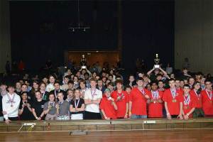 Students from the top three teams celebrate at the Science Olympiad 2026 awards ceremony, smiling and cheering while holding medals and trophies