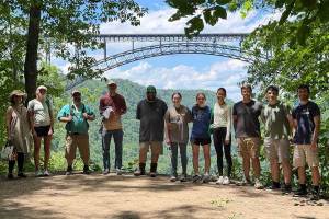 Participants in Marshall University's Appalachian Mathematics and Physics Site (AMPS) summer research program stand on a trail overlook at New River Gorge National Park with the New River Gorge Bridge in the background