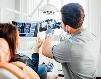 Consultation showing a dental professional reviewing an X‑ray image with a seated patient, discussing findings related to teeth and oral health