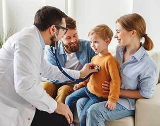 Clinical exam showing a physician assistant using a stethoscope to listen to a child’s chest while the child sits with caregivers during a routine checkup