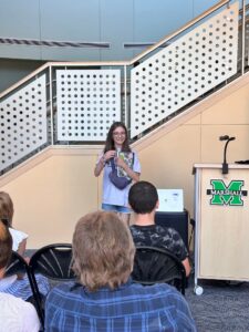girl reading her story at a podium to an audience in a library