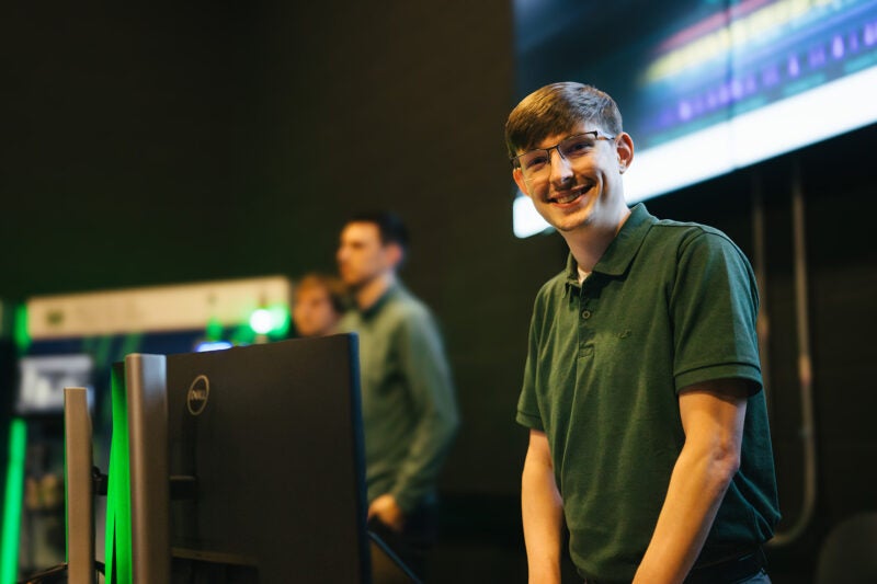 a student smiles at the camera while standing in front of a computer in a lab