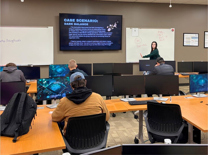 Students work on computers during a Cyber Experience event while an instructor gives directions at the front of the room