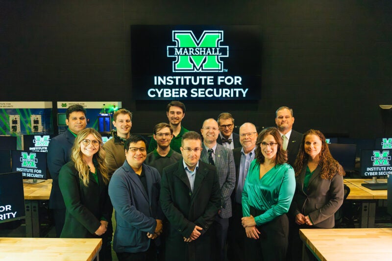 Marshall Institute for Cyber Security staff stand together for a photo in a computer lab with the ICS logo behind them.