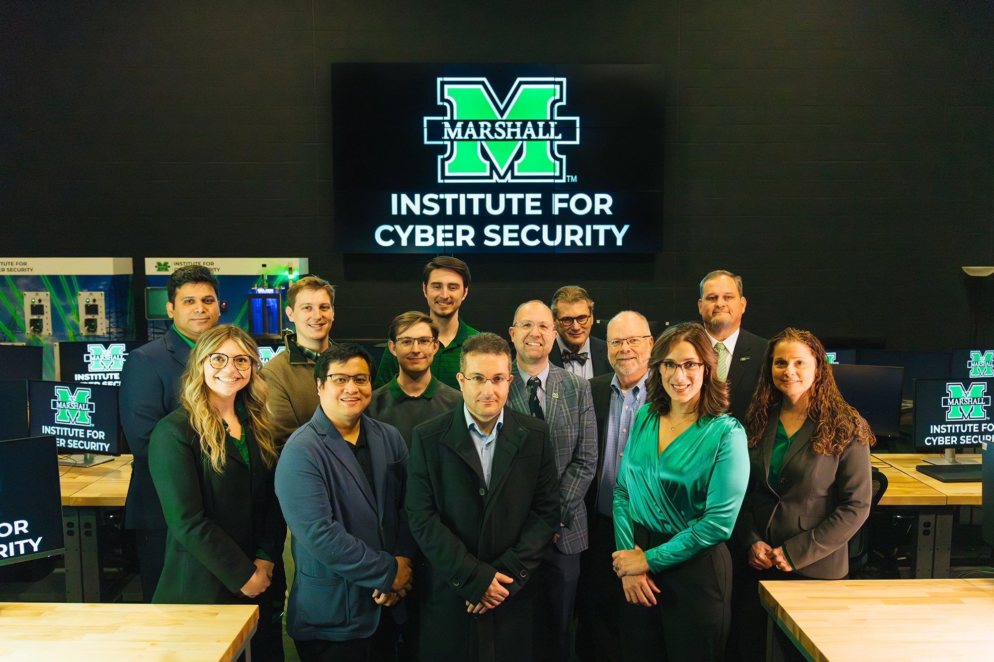 Marshall Institute for Cyber Security staff stand together for a photo in a computer lab with the ICS logo behind them.