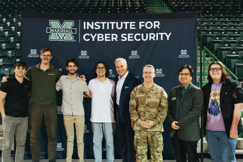 A group of people smile for a photo in front of a Marshall University Institute for Cyber Security backdrop