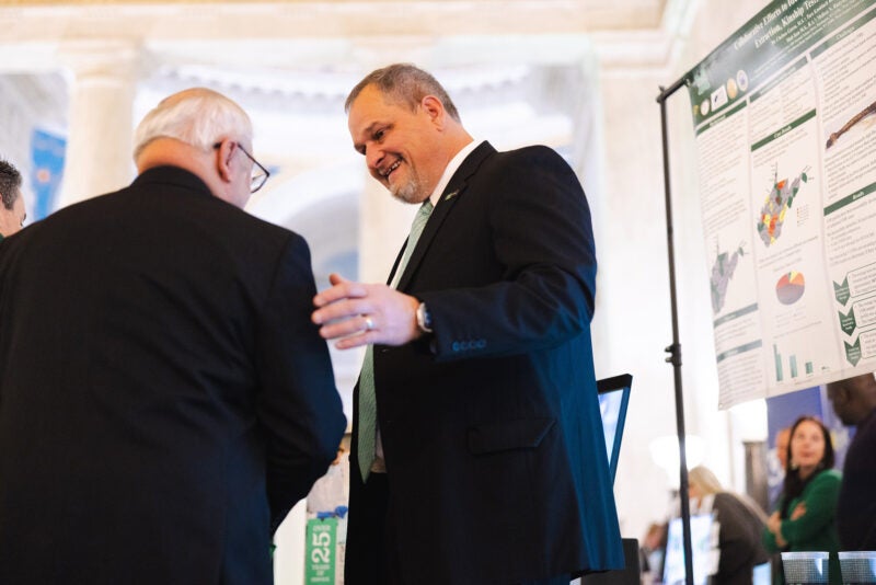 Two men in suits talk to each other with a cyber research poster behind them