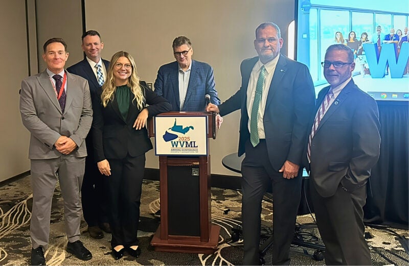 A group of attendees smile for a photo around a podium with a WVML Annual Conference sign on it