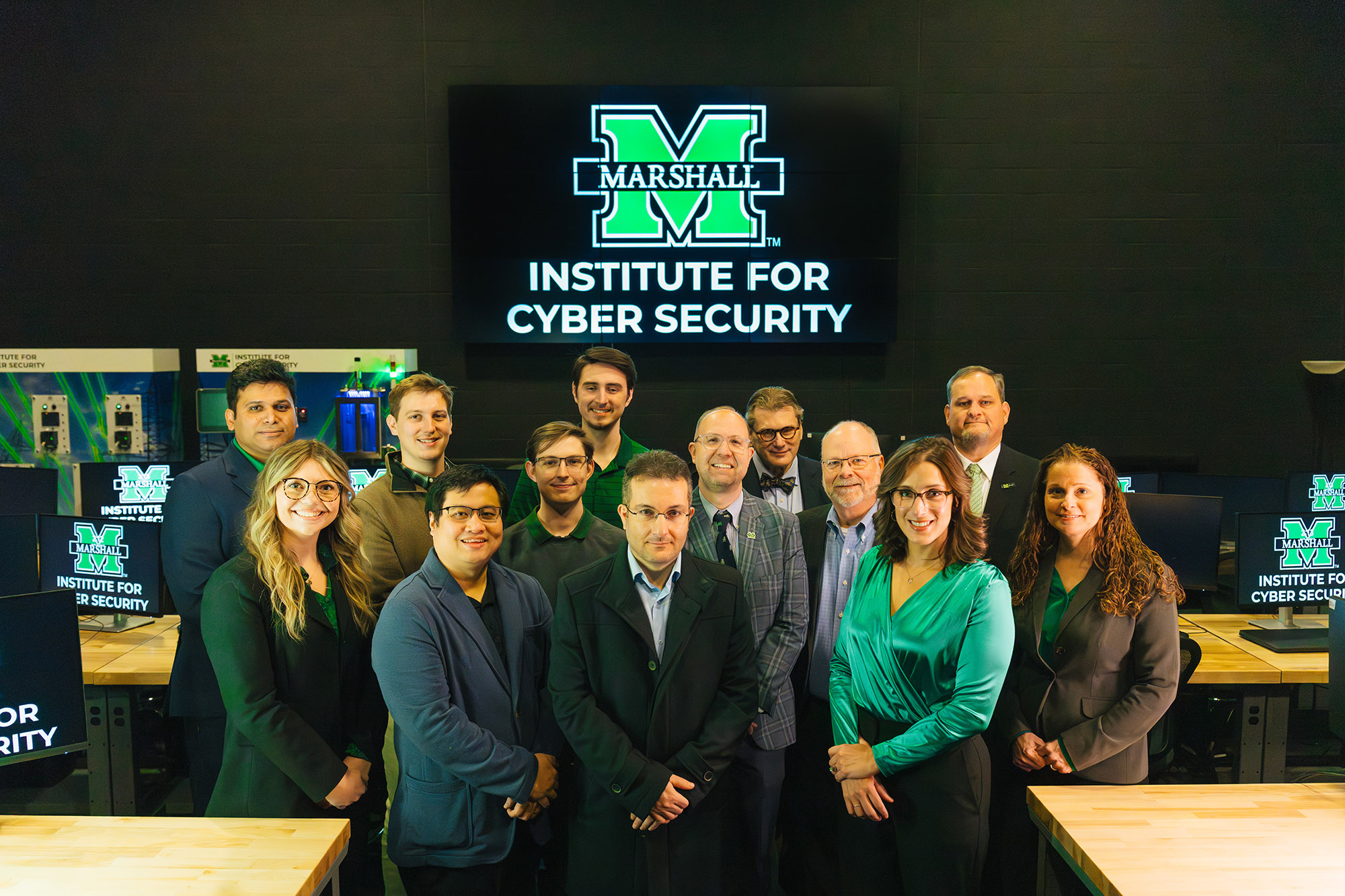 Marshall Institute for Cyber Security staff stand together for a photo in a computer lab with the ICS logo behind them.