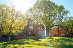 Old Main with sunlight beaming down and trees in bloom in Spring 2024.
