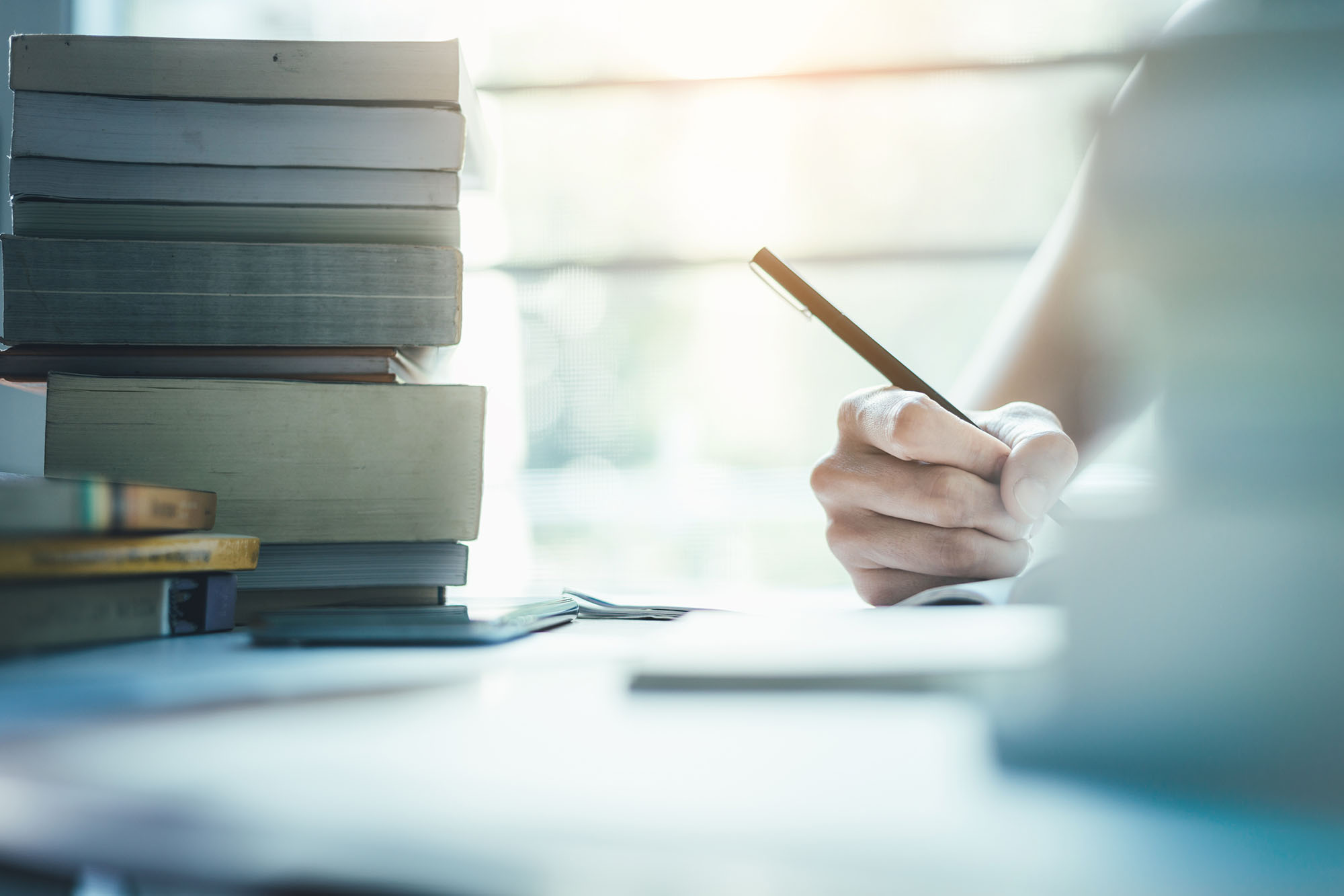 Image of someone writing surrounded by books on the table