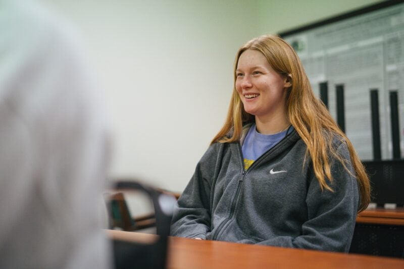 student sitting in a lecture hall at a desk and smiling