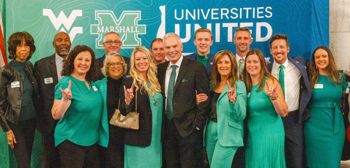 Attendees wearing green and black gather together for a group photo in front of the Universities United backdrop.