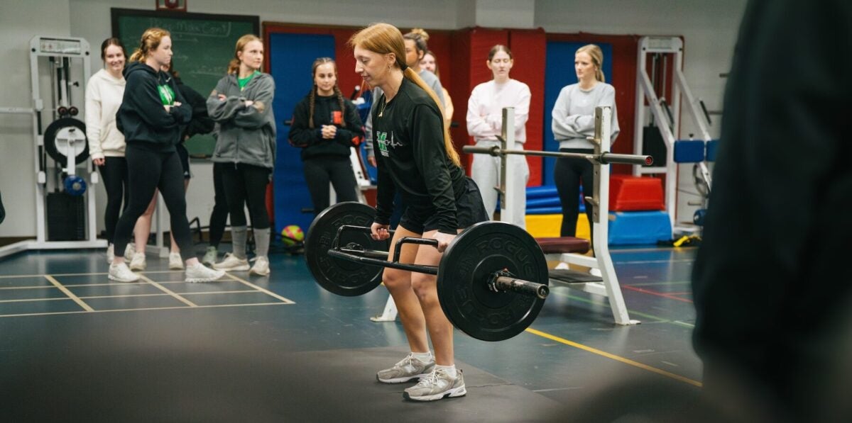 student doing a squat with a weight bar in the exercise science lab