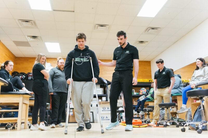 student on crutches being supervised by another student