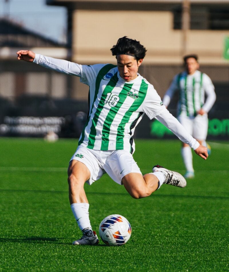 Marshall soccer player about to kick the ball on the field with his arms stretched out to the sides