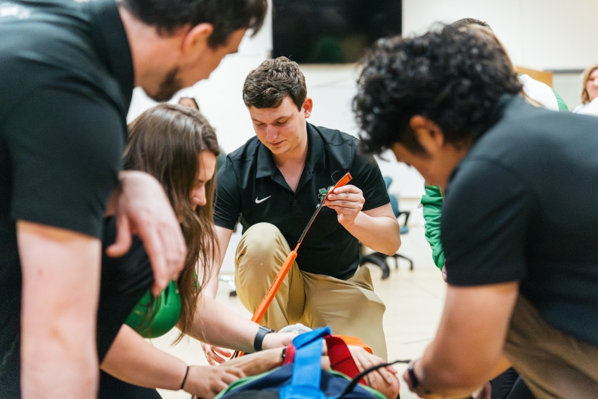 four students working on putting a patient on a back board in an athletic training lab