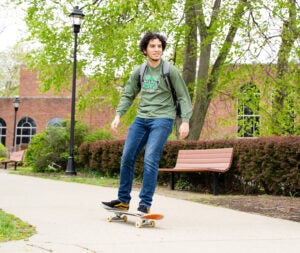 Male student skateboarding wearing blue jeans and a green MU shirt
