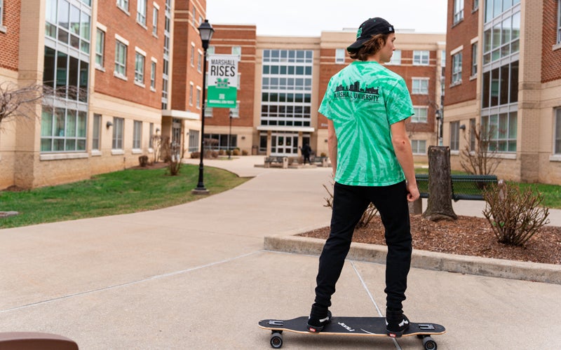 A student rides a skateboard outside of Marshall Commons