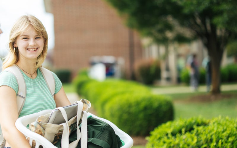 A student carries a basket of items while moving into Marshall University's residence halls