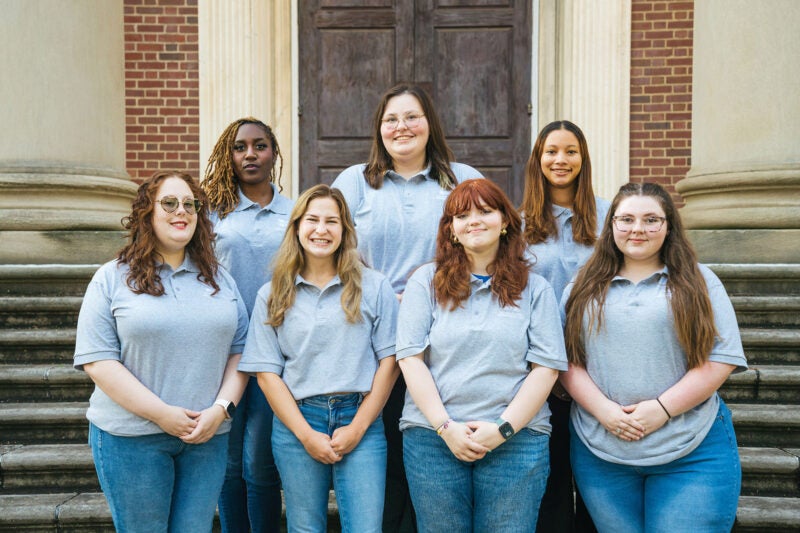 Buskirk Hall staff members wear matching gray shirts and smile together on the steps of Morrow Library