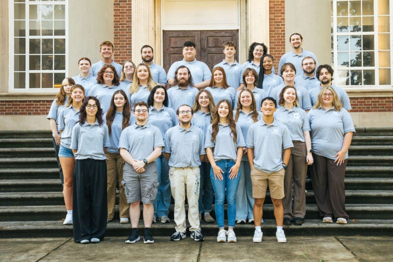 Staff members from Marshall's Towers Residence Halls wear matching gray shirts and smile together on the steps of Morrow Library