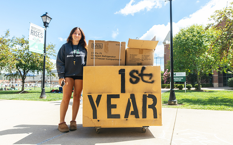 Student stands outside of the residence halls with a cart during move-in