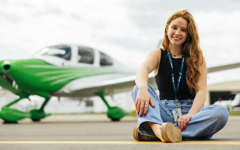 A Marshall University Aviation student sits in front of a Marshall branded plane