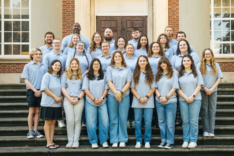 Staff members from Marshall's First Year Residence Halls wear matching gray shirts and smile together on the steps of Morrow Library